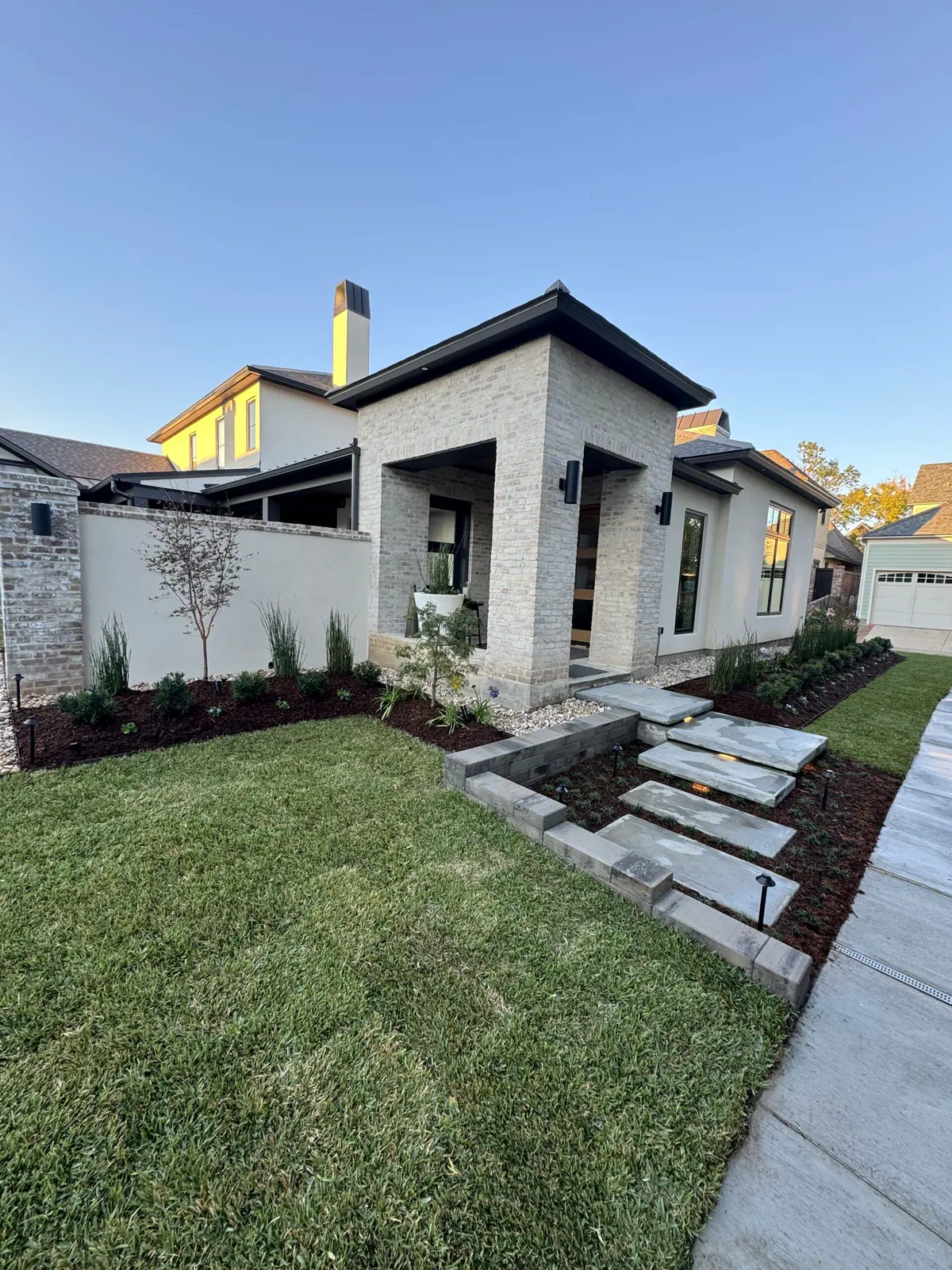 Front walk of pavers between planting beds and an artificial turf lawn